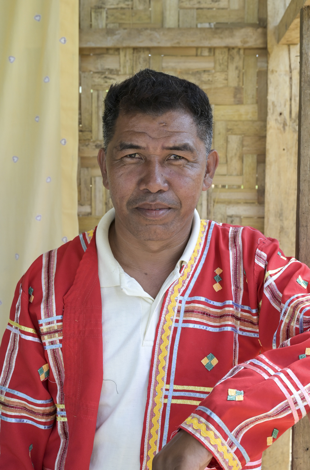 Porträt des Dorfvorstehers Alan Otti. Er trägt eine mit traditionellen Mustern verzierte, rote Jacke.