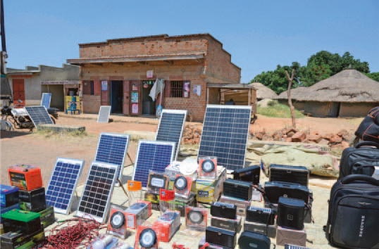 Ein Stand, der direkt an der Straße verschiedene Waren anbietet, darunter Solarpanele in verschiedenen Größen. Dahinter der eigentliche Shop in einem unverputzen, einstöckigen Gebäude.