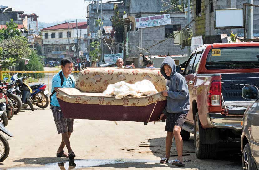 Zwei Männer tragen ein Sofa aus der zerstörten Stadt Marawi in Richtung eines Autos mit Ladefläche.
