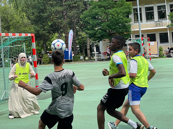 Torszene beim missio Unity-Cup: Drei Jungs laufen auf die Torwärterin im Hidschab zu, vor ihnen in der Luft der Fußball.