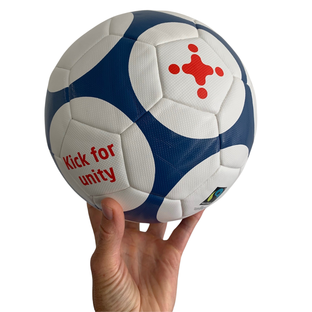 Eine Hand hält einen missio-Fussball mit Fairtrade-Logo und dem Aufdruck "Kick for Unity"