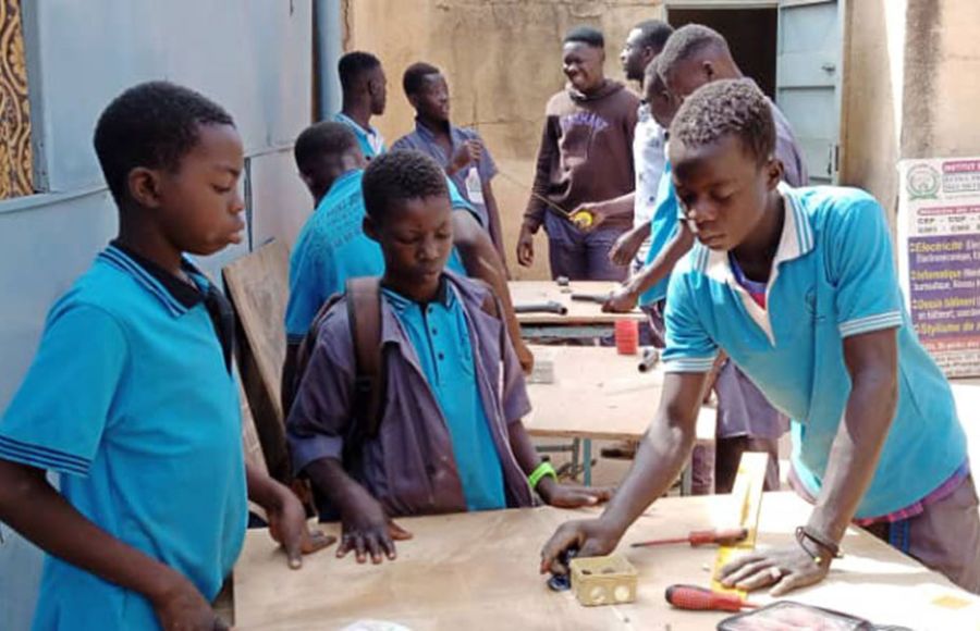 Jugendliche in Burkina Faso erlernen ein Handwerk: im Vordergrund stehen drei Jugendliche in hellblauen T-Shirts an einer Werkbank.