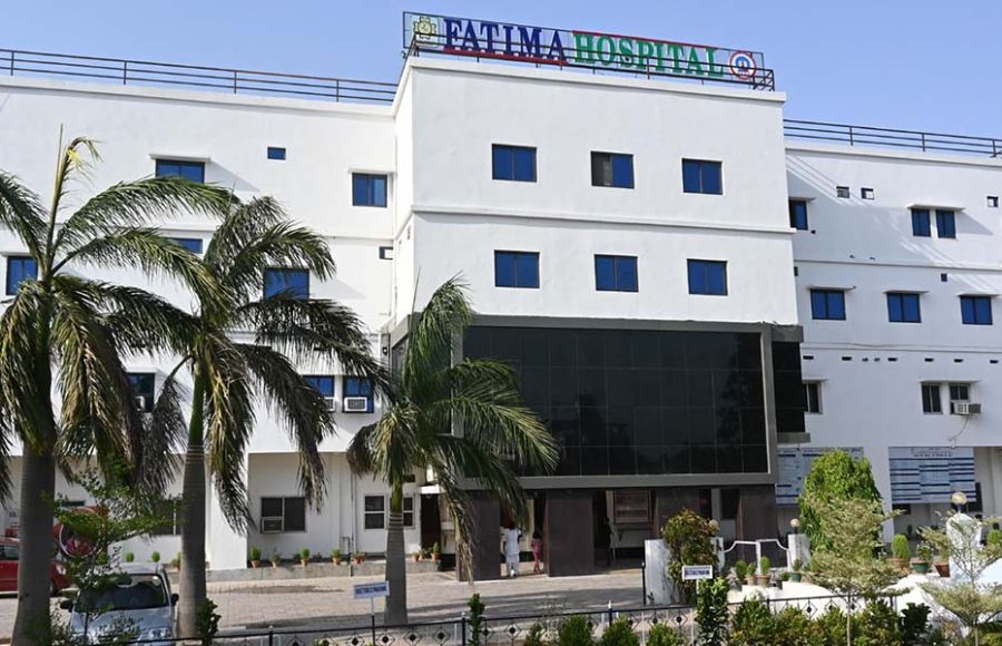 Zu sehen ist das Fatima Krankenhaus, ein großes weißes, rechteckiges Gebäude mit drei großen Palmen im Vordergrund.
